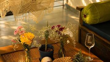 Ein Hängesessel, ein Holztisch mit einem Buch, Obst, Blumen und einem Weinglas.