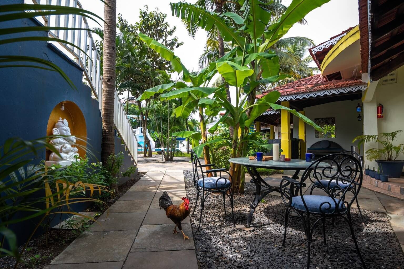Un patio con una mesa, sillas, una estatua y un gallo.