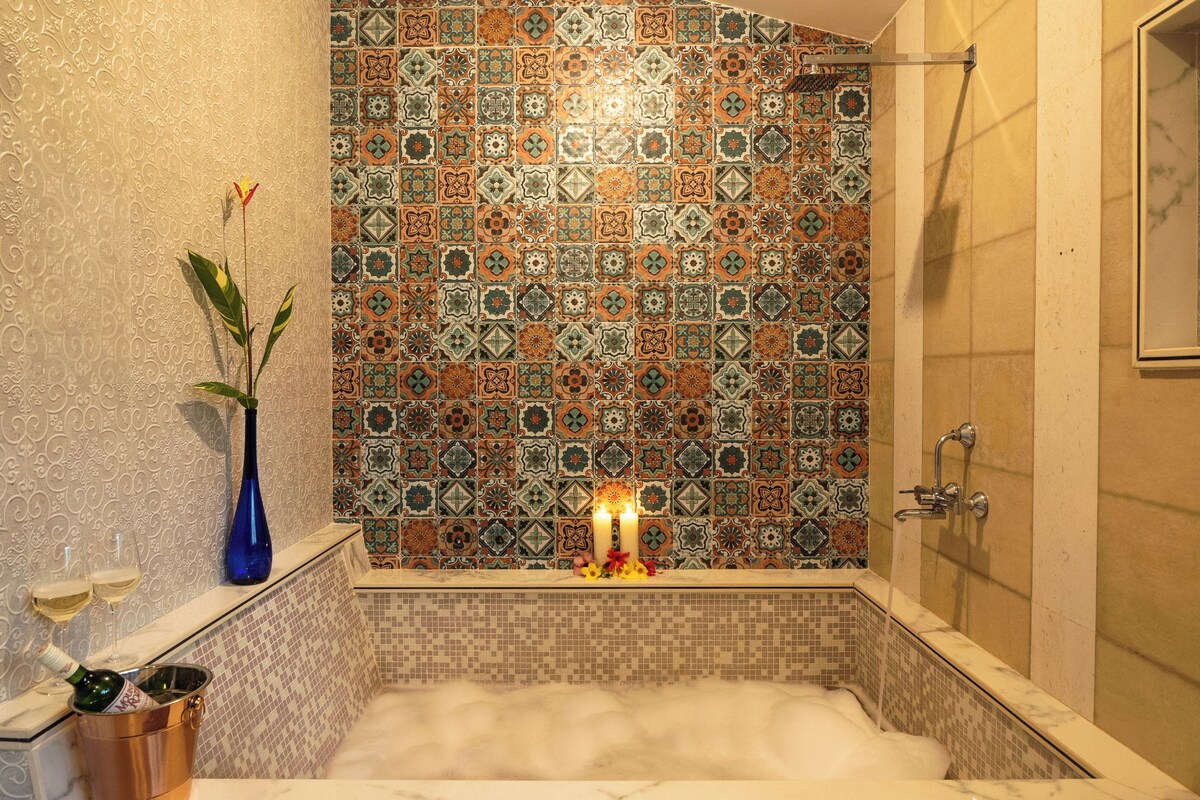 A bathroom with a tiled wall, a bathtub, a shower, and a vase with flowers.