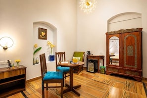A hotel room with a dining area, a minibar, and a large wooden wardrobe. - Sashas Holiday Village (Vagator)