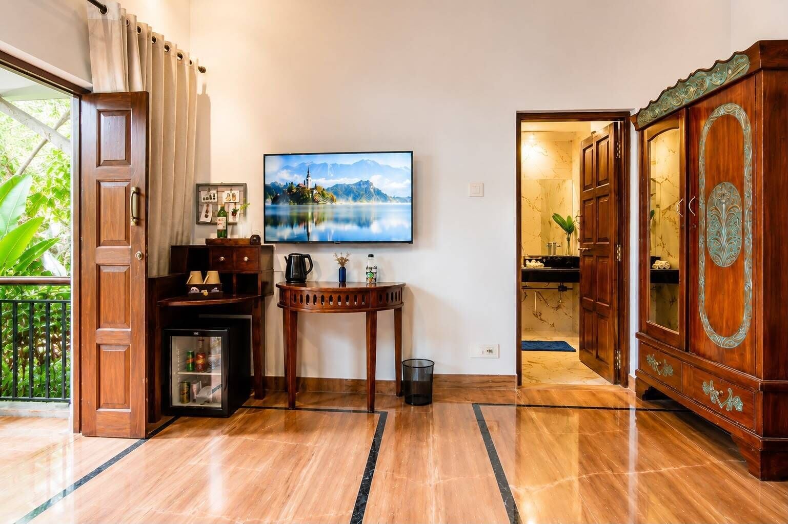 Una habitación con un armario de madera, un televisor fijado a la pared y una mesita con una tetera y una botella.