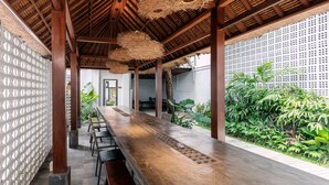 A long wooden table with chairs, a woven ceiling, and a garden with tropical plants. - Chandi Hotel Ubud  (Ubud)