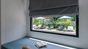 A window seat with a view of a garden area, a book, and a hat. - Chandi Hotel Ubud  (Ubud)