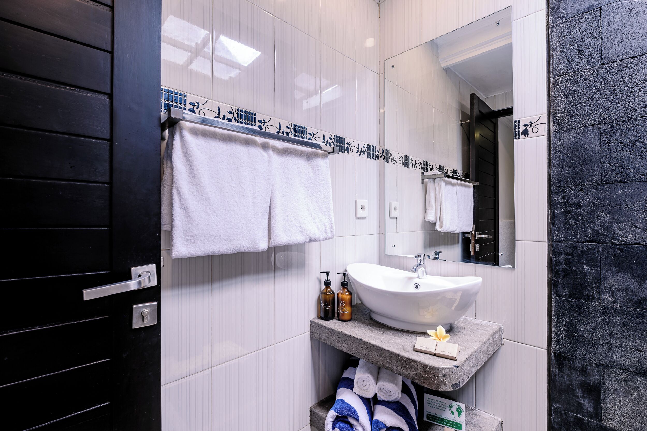 A modern bathroom with a white sink, black and white tiled walls, a large mirror, and neatly hung towels.