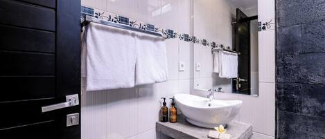 A modern bathroom with a white sink, black and white tiled walls, a large mirror, and neatly hung towels.
