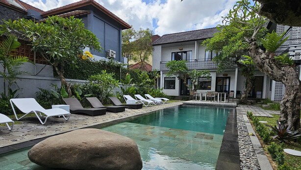 A pool area with lounge chairs, a rock in the water, and a building with a tiled facade. - Chandi Hotel Ubud  (Ubud)