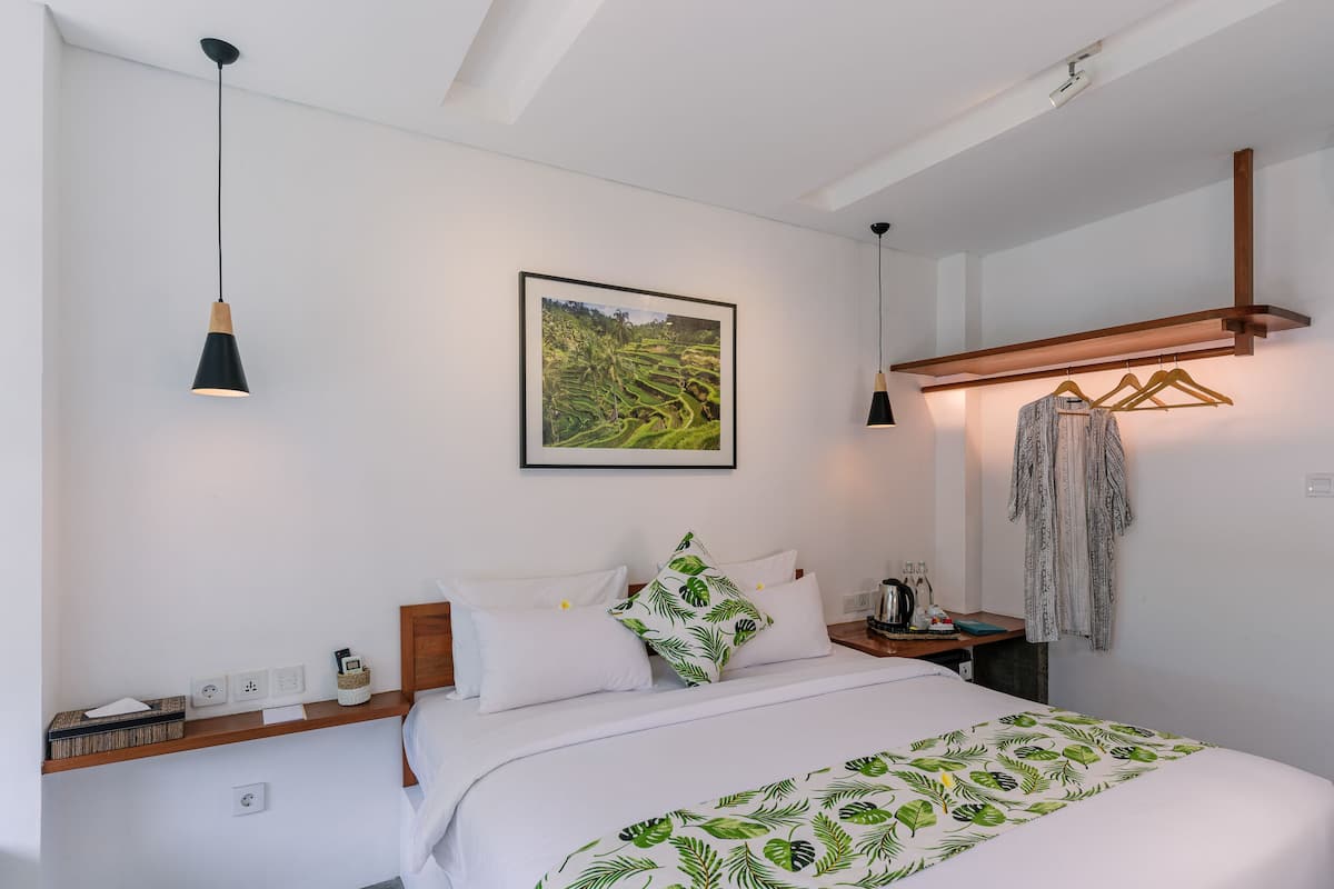 A neatly arranged hotel room with a bed, bedside table, and a wall-mounted coat rack.