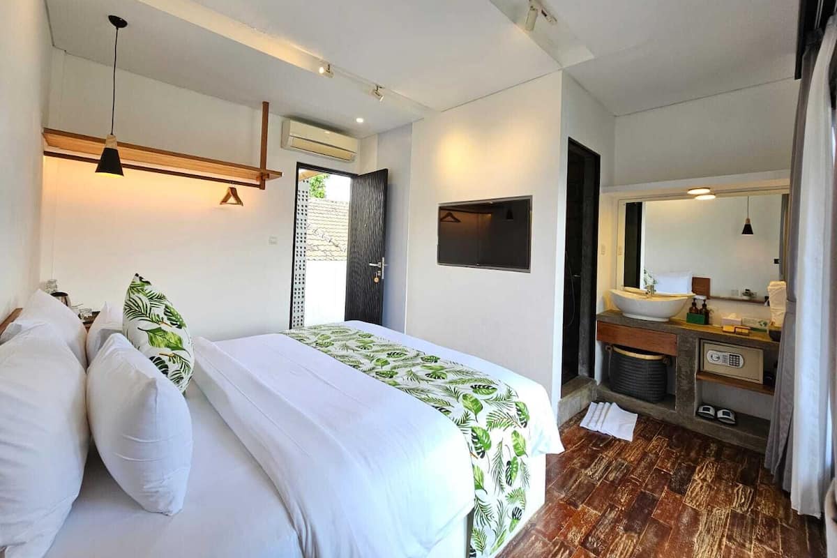 A modern bedroom with a bed, a bedside table, a mirror, and a bathroom with a sink and shower.