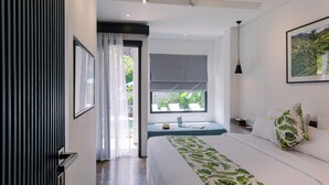 A modern hotel room with a large bed, a view of greenery outside, a laptop on a bedside table, and a framed picture on the wall. - Chandi Hotel Ubud  (Ubud)