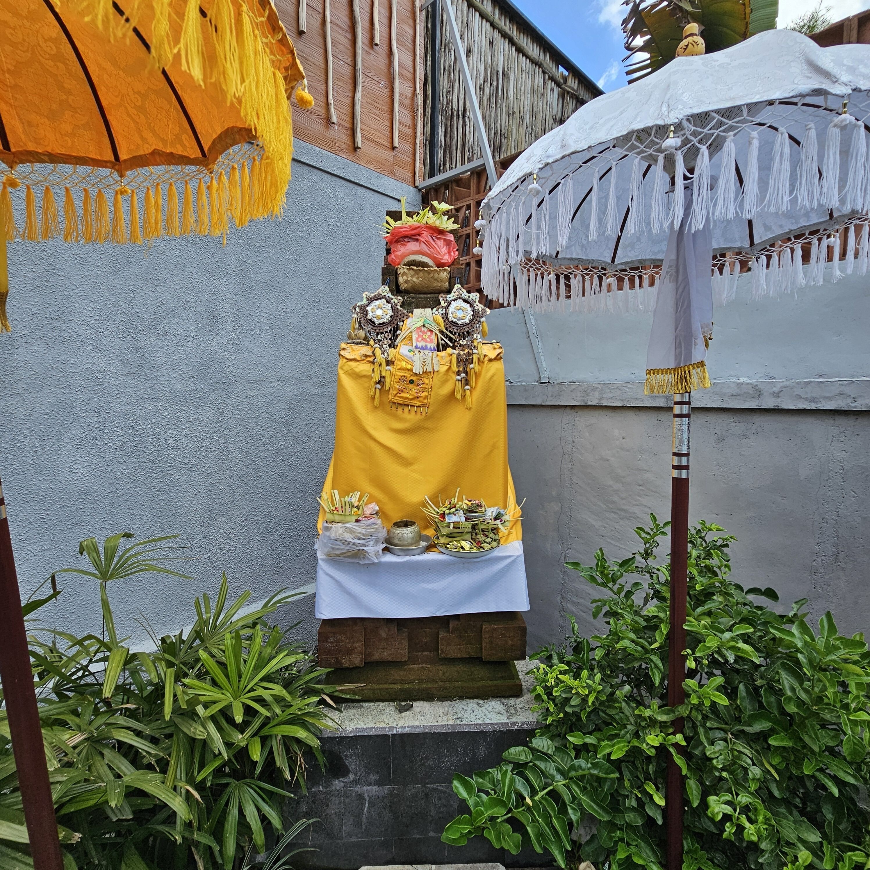 Una estatua de una deidad adornada con joyas intrincadas y un paño amarillo, colocada sobre un pedestal con ofrendas delante.