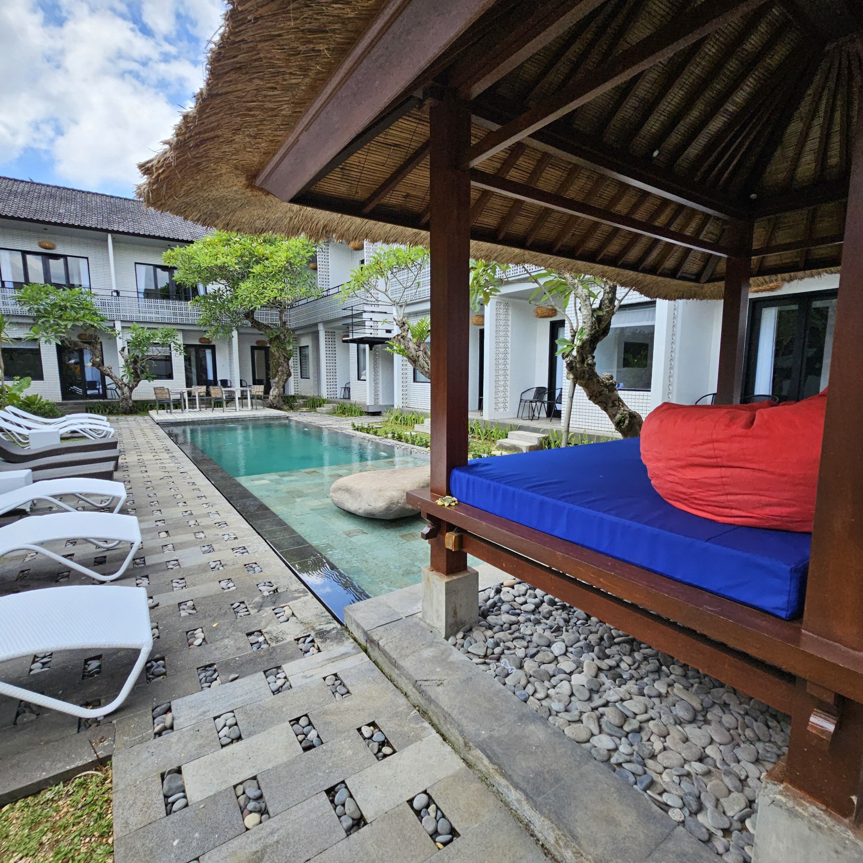 A poolside area with lounge chairs, a small pool, and a covered seating area with a red cushion.