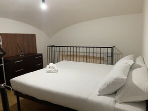 Quarto com uma cama, cômoda de madeira e parede branca.