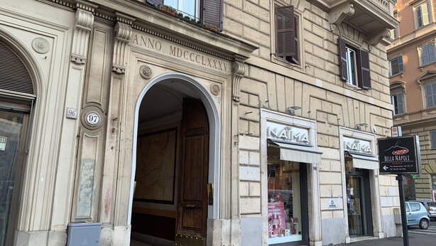 A building with a classical facade, featuring an arched entrance and a storefront with a 'NAIMA' sign.