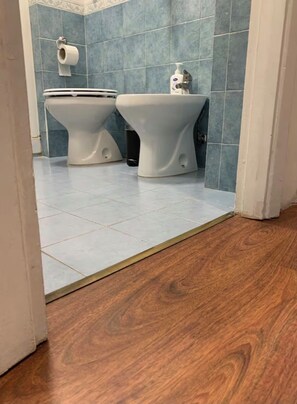 Casa de banho com duas sanitas, suporte para papel higiénico e dispensador de sabonete líquido na parede.