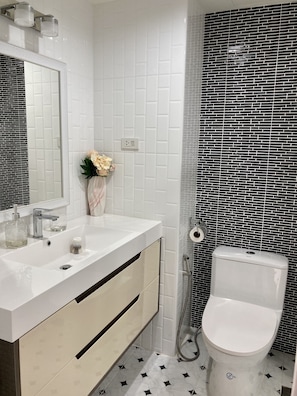A bathroom with a white sink, mirror, and toilet. There is a shower with a black and white patterned wall. - Paradise Condominium by PSR (Pattaya)