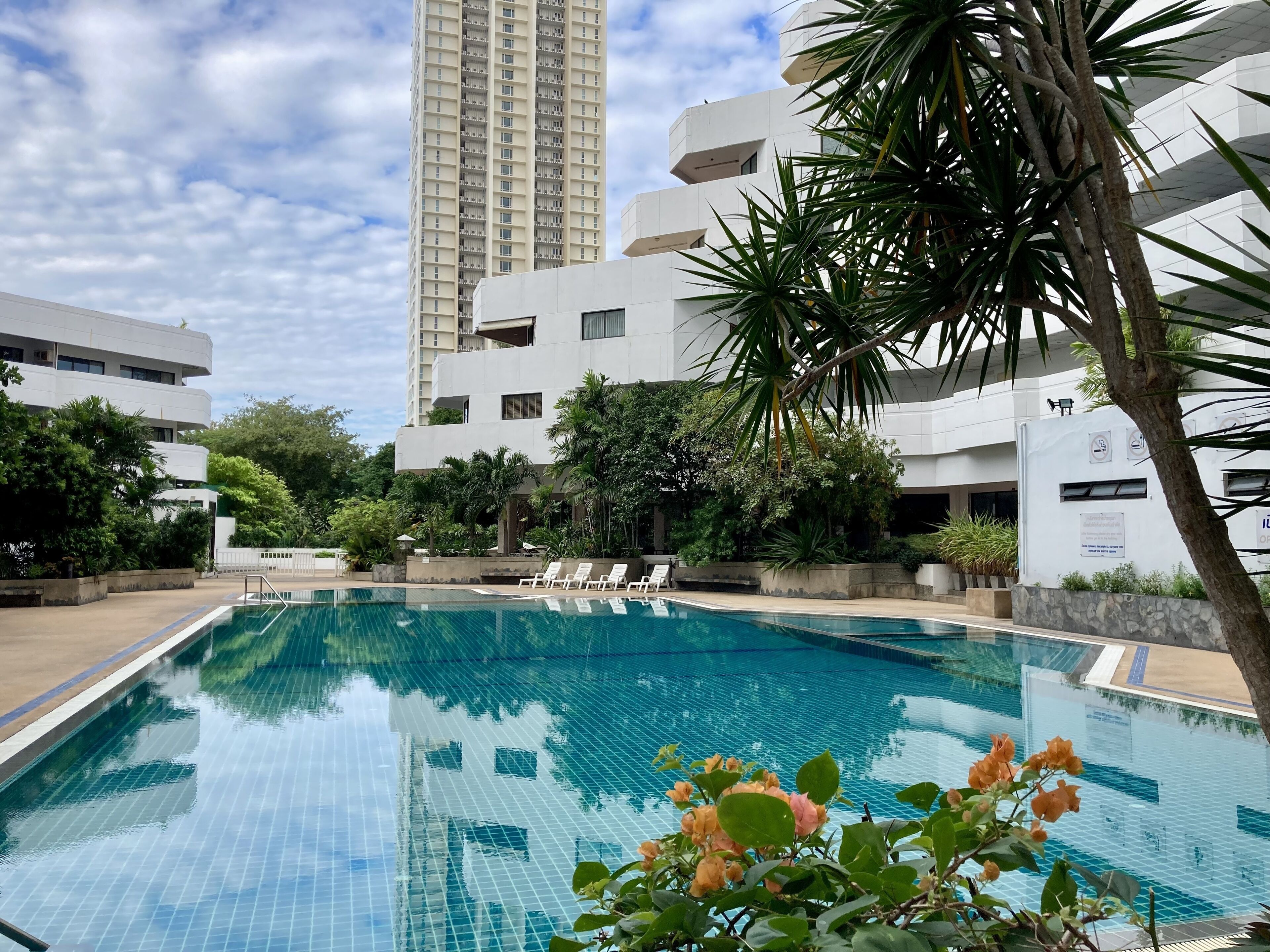 A swimming pool with clear blue water, surrounded by lush greenery and modern buildings.