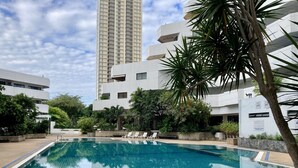 Una piscina con agua cristalina azul, rodeada de exuberante vegetación y edificios modernos.