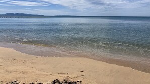 Una playa con agua cristalina, una orilla arenosa y montañas a lo lejos.
