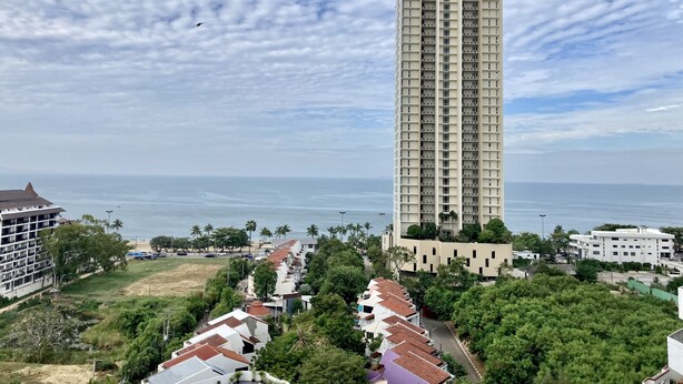 Un edificio residencial alto con varios balcones, rodeado de vegetación y vistas al mar.