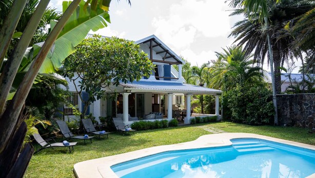 Une maison avec une piscine, entourée d’une végétation luxuriante et de palmiers.