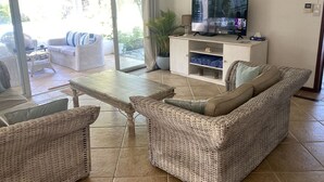 Un salon meublé avec des meubles en osier, un téléviseur et une porte-fenêtre coulissante donnant sur l’extérieur.