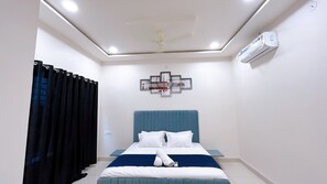 A bedroom with a bed, a ceiling fan, an air conditioner, and a wall-mounted artwork. - Home Escape Luxe (Ujjain)