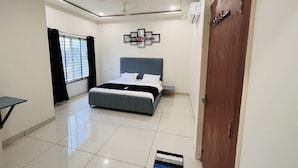 A bedroom with a bed, a ceiling fan, a wall-mounted air conditioner, and a door with a coat rack. - Home Escape Luxe (Ujjain)