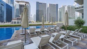 A rooftop pool area with lounge chairs and umbrellas, overlooking a cityscape with modern high-rise buildings. - Two Bed Room 5 minutes to Burj Khalifa & Dubai Mall-DAMAC REVA Residence 2705 (Dubai)