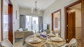 A modern hotel room with a dining area, a sofa, a TV, and a city view. - Two Bed Room 5 minutes to Burj Khalifa & Dubai Mall-DAMAC REVA Residence 2705 (Dubai)