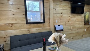 Un interior de madera con un sofá, una mesa con un jarrón y una botella, y una ventana con vistas a árboles.