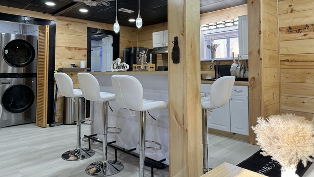 Una cocina moderna con paredes de madera, electrodomésticos de acero inoxidable, taburetes de bar blancos e iluminación colgante.