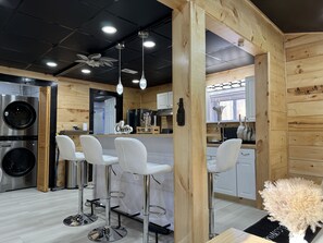 A modern kitchen with wooden walls, stainless steel appliances, white bar stools, and pendant lighting. - Modern stylish cabin locate at White Mountain near Franconia unit 2 (Bethlehem)
