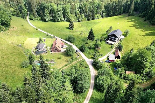 An aerial view of a rural property with a winding road, a barn, a house, and a swimming pool. - Forsthaus | Grillplätze | Sauna | Zaun | Multifunktionsraum (Forbach)
