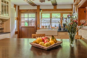 A wooden kitchen with a fruit bowl on the table, a vase with flowers, and a window with a view of greenery. - Forsthaus | Grillplätze | Sauna | Zaun | Multifunktionsraum (Forbach)
