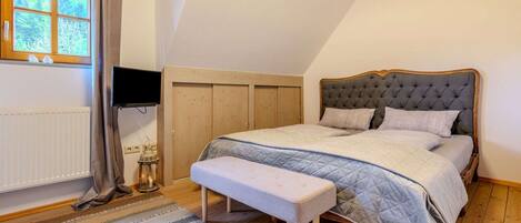 A bedroom with a large bed, a bench, a TV, and a window with curtains.
