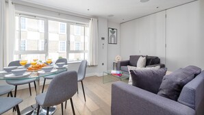 Ein modernes Wohnzimmer mit einem Glastisch, grauen Sofas und einem großen Fenster mit Vorhängen.