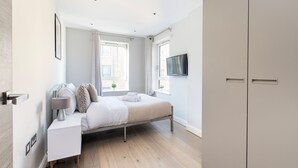 Ein modernes Schlafzimmer mit Bett, Nachttisch und Fernseher an der Wand.