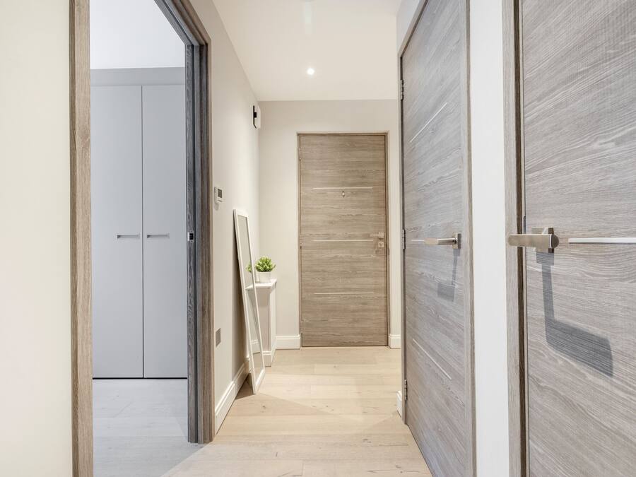 A hallway with a wooden door, a small plant on a white pedestal, and a mirror leaning against the wall.