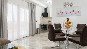 A modern dining area with a glass table and brown chairs, a kitchen in the background, and a large window with curtains. - Villa My Dream in Kastel Stari (Kastela)