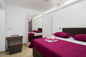 A modern bedroom with a large mirror, a bedside table, a bed with a pink bedspread, and a chandelier.