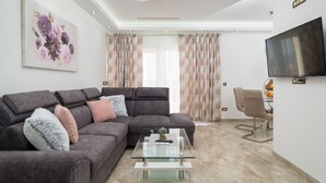 A modern living room with a sectional sofa, a glass coffee table, and a flat-screen TV mounted on the wall. - Villa My Dream in Kastel Stari (Kastela)