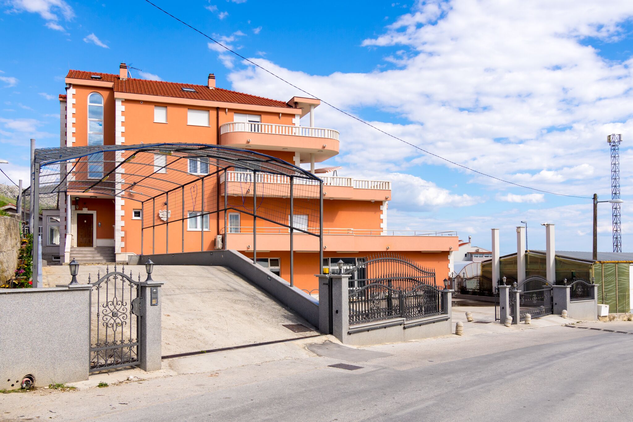 Un edificio residencial de varios pisos con entrada protegida por un portón y una escalera que conduce a ella, bajo un cielo despejado.