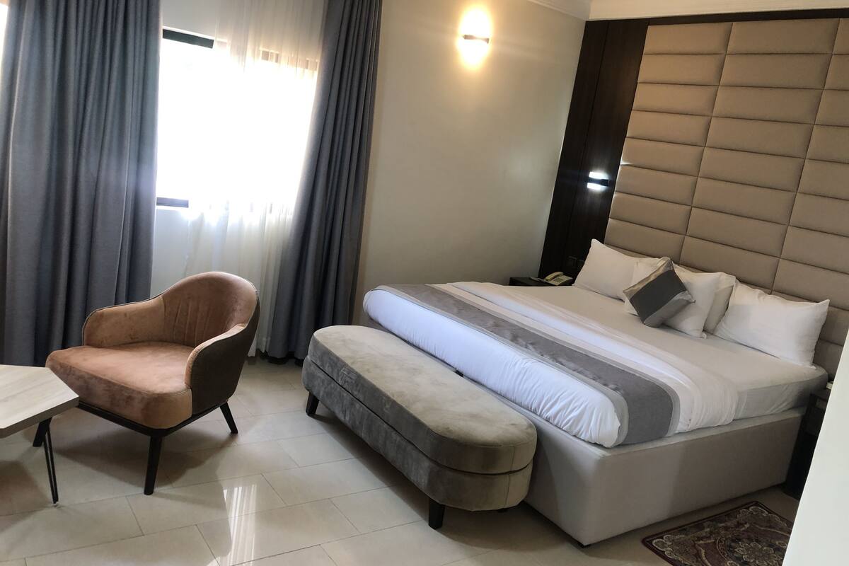 Une chambre d’hôtel comprenant un lit, une chaise, une table de chevet et une petite table de nuit avec un téléphone.