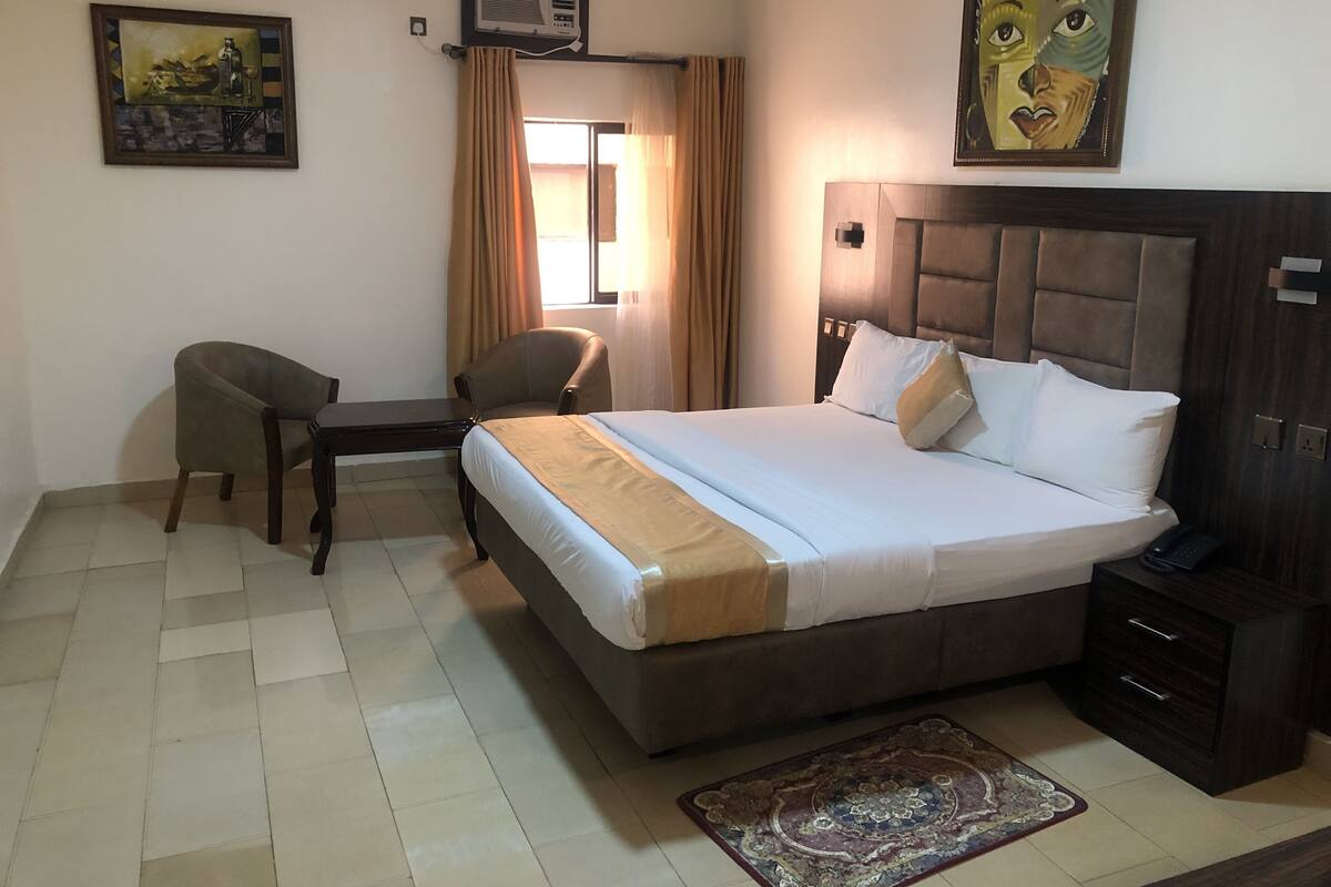 Une chambre d’hôtel équipée d’un lit, d’un bureau, d’une chaise, d’une table de chevet et d’un climatiseur fixé au mur.