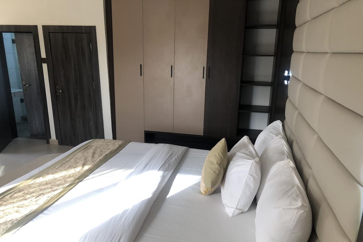 Une chambre à coucher avec un lit, des oreillers beiges et blancs, une tête de lit et une armoire.