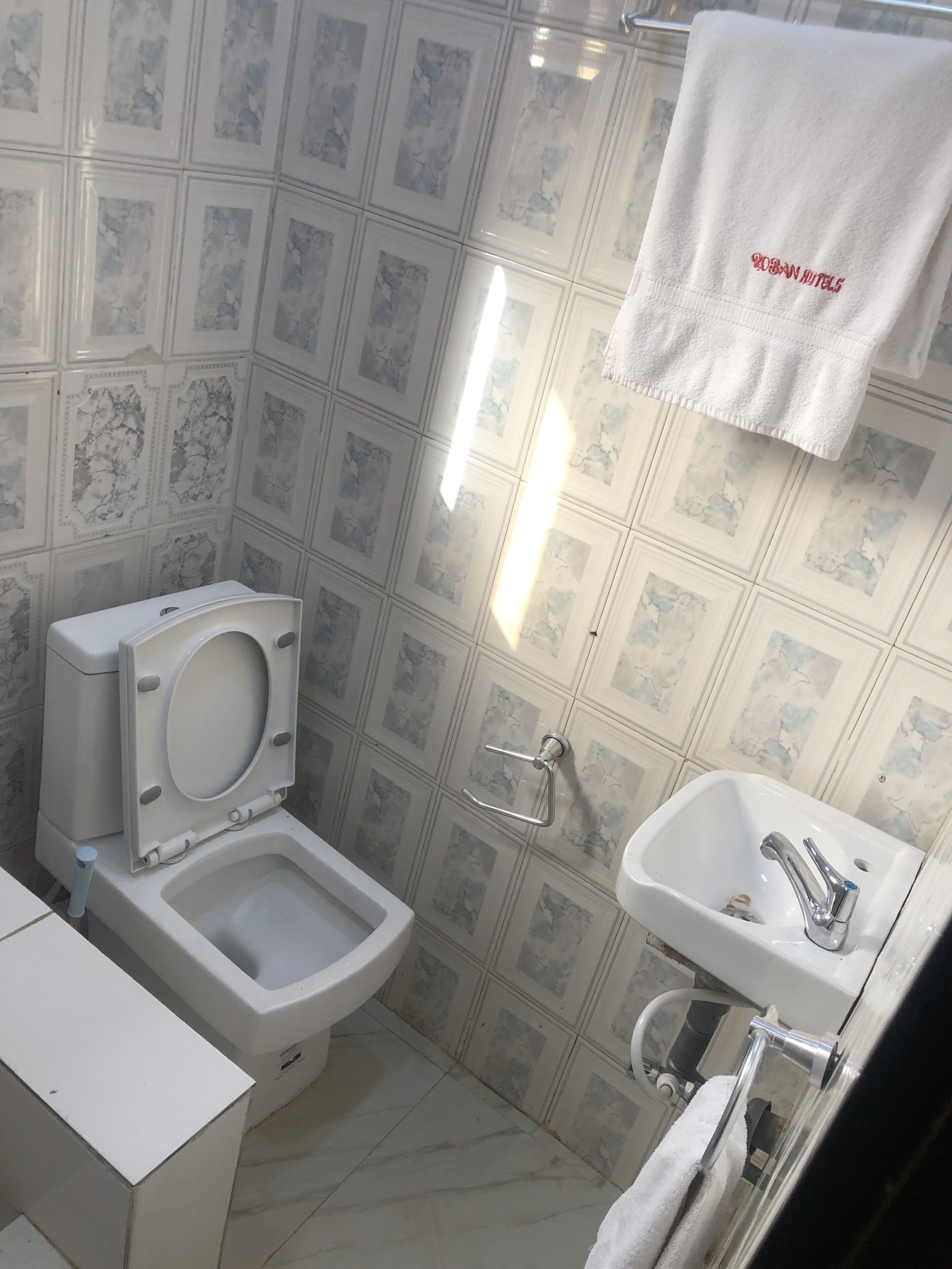 A bathroom with a toilet, sink, and a towel hanging on the wall.