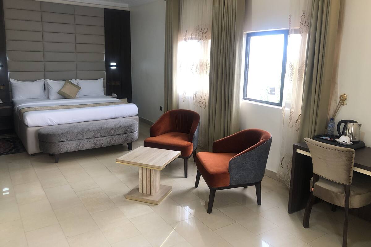 Une chambre d’hôtel comprenant un lit, deux fauteuils, une petite table et un bureau avec une chaise.