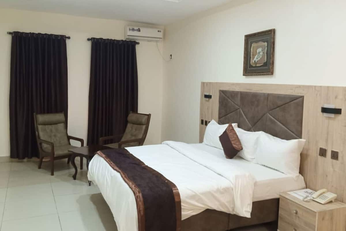 Une chambre d’hôtel comprenant un lit, deux chaises, une table de chevet avec un téléphone et un appareil de climatisation.