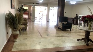 A spacious lobby with a marble floor, a reception desk, and a seating area with a chair and a table. - Roban Hotels Limited (Enugu)