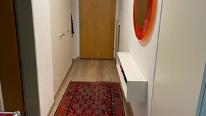 A hallway with a wooden door at the end, a white console table, and a red patterned rug. - Ferienwohnung Waldrand EG by Interhome (Lenk)